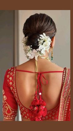 the back of a woman's red blouse with flowers in her hair and an elaborate necklace