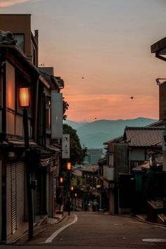 an alley way with buildings and mountains in the background at sunset or sunrise, as seen from across the street