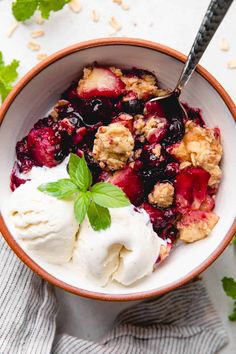 a bowl filled with fruit and ice cream on top of a white table next to green leaves