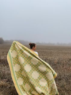 a woman standing in a field holding a quilt