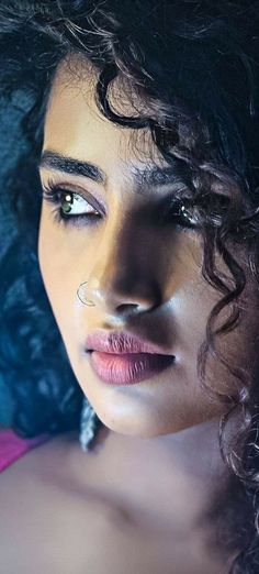 a close up of a woman with curly hair and makeup on her face, looking at the camera