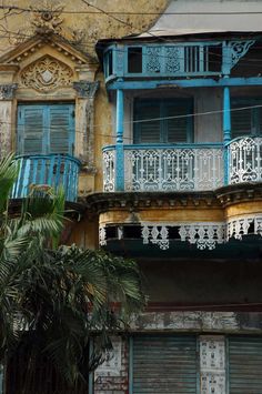 an old building with blue and white balconies on the second story, next to a palm tree