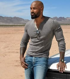 a bald man leaning on the hood of a car in the middle of an empty desert