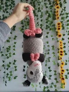 a person holding up a crocheted stuffed animal hanging from a string with flowers in the background