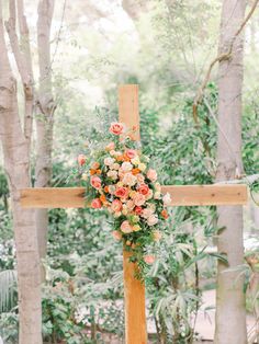 a cross decorated with flowers and greenery for a wedding ceremony in an outdoor setting