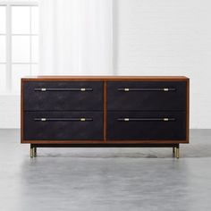 a black and brown dresser with brass handles in an empty room next to a window