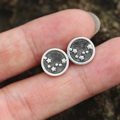 a person's hand is holding two small silver studs with stars on them