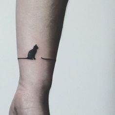 a small black cat sitting on top of a person's leg with a tiny tattoo