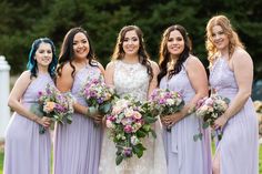 a group of women standing next to each other holding bouquets and smiling at the camera