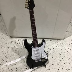 a black electric guitar sitting on top of a white counter next to a ribbon holder