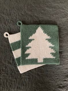 two green and white crocheted christmas tree coasters on a black tablecloth