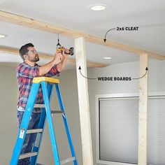 a man standing on a ladder working on the ceiling in a room with white walls