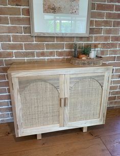 a wooden cabinet with wicker doors in front of a brick wall and wood floor