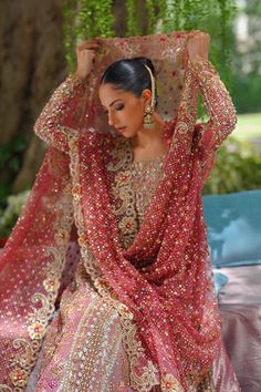 a woman in a red and gold bridal dress sitting on a bench under a tree