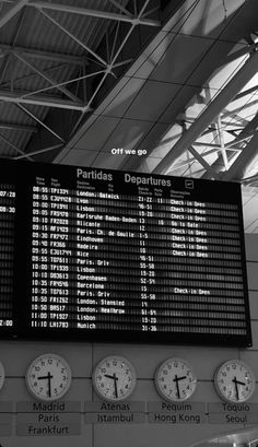 an airport departure board with several clocks on the wall and in front of it, there is a list of departures