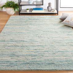 an area rug in the middle of a living room with pillows and bookshelf