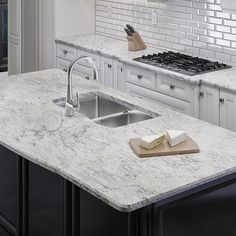 a kitchen with white marble counter tops and black cabinets, along with a sink that has a cutting board on it