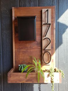 a wooden clock mounted to the side of a wall next to a potted plant