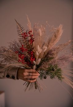 a person holding a bunch of flowers with red berries and greenery in their hands