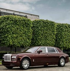 a rolls royce parked in front of a building with trees on the side and bushes behind it