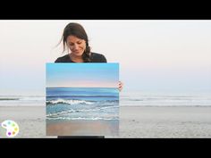 a woman holding up a painting on the beach