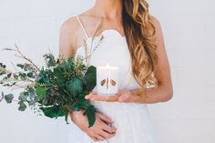 a woman holding a white candle with greenery