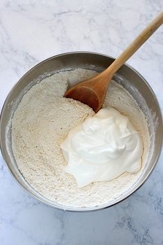 a wooden spoon in a metal bowl filled with flour and whipped cream on a marble counter top