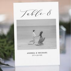 a table card with an image of two people walking on the beach and pine branches in the background