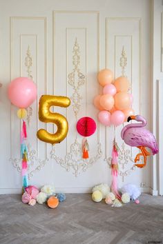 balloons and flamingos are arranged on the floor in front of a number five sign