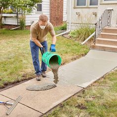 a man is pouring cement into a bucket on the sidewalk in front of a house