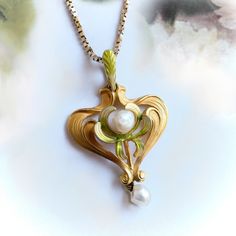 "Found is this beautiful gold and pearl lavalier pendant from the Art Nouveau (ca 1910) era. This delicate piece is made of vibrant, brushed 14k yellow gold and has a flowing stylized heart shape approx. 32 mm long x 21 mm wide x ⅛\" thick. The pendant has a leaf motif with delicate, leaf-like swirls adorned with soft enameling in hues of green and yellow. In the center of the pendant is a single freshwater pearl.  Dangling freely from the base of the pendant is another l4.2 mm x 5mm  pearl. The Gold Art Deco Necklace With Pearl Pendant, Art Nouveau Yellow Gold Jewelry Gift, Collectible Art Nouveau Yellow Gold Jewelry, Art Deco Pearl Pendant Jewelry For Gift, Victorian Yellow Gold Heart Pendant Necklace, Vintage Heart Pendant Jewelry With Pearl, Art Nouveau Pearl Pendant Jewelry For Wedding, Art Nouveau Yellow Gold Pendant Jewelry, Art Nouveau Wedding Jewelry With Pearl Pendant