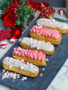 four pastries with pink and white frosting on a black tray next to candy canes