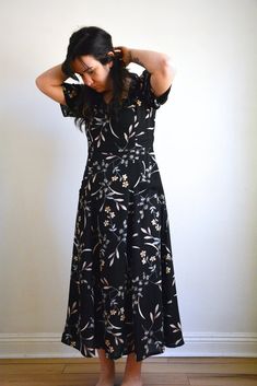 a woman standing in front of a white wall wearing a black floral dress with short sleeves