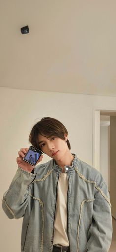 a young man is taking a selfie with his cell phone while wearing a denim jacket