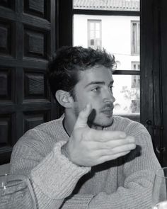 a black and white photo of a man sitting at a table in front of a window