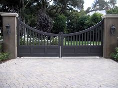 an iron gate and brick walkway leading to a driveway