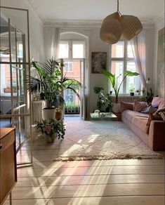 a living room filled with lots of furniture and plants on top of a hard wood floor