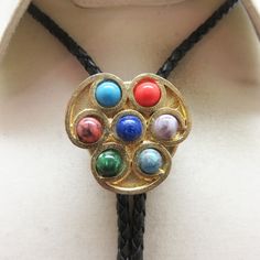 This cool Faux Gemstone bolo tie works for a woman with a sense of style. It is goldtone metal with small semiprecious cabochons in excellent condition. It measures 1 3/8ths inches tall by 1 3/8ths inches wide. It is placed on a brand new 36 inch long braided black leather string tie with  goldtone metal end caps. All pieces are in great condition.  This was handmade in our very own Montana rock shop, Rockin' JK Designs.  We will mail this to you in a lovely gift box for easy gift giving or safe Gold Adjustable Cord Bolo Ties For Gift, Adjustable Gold Bolo Tie As Gift, Adjustable Southwestern Gold Jewelry, Gold Bolo Ties With Adjustable Cord As Gift, Gold Bolo Ties With Adjustable Cord For Gifts, Adjustable Multicolor Necklace For Formal Occasions, Vintage Lariat Jewelry With Sliding Knot, Gold Lariat Bolo Tie With Adjustable Length, Vintage Jewelry With Adjustable Length For Formal Occasions