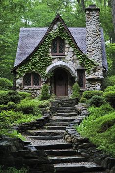 a stone house with steps leading up to the front door and windows, surrounded by greenery