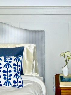 a bed with blue and white pillows on top of it next to a night stand