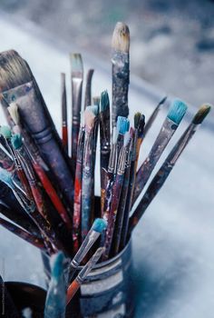 a cup filled with lots of paintbrushes sitting on top of snow covered ground