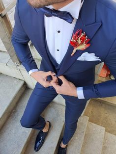 a man in a blue suit and bow tie is standing on steps with his hands in his pockets