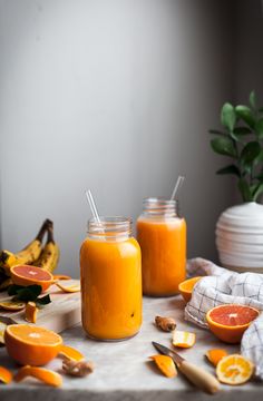 two jars filled with orange juice sitting on top of a table next to sliced fruit