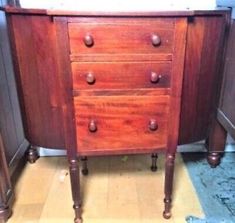 an old wooden dresser with drawers and knobs on the bottom, in front of a wall