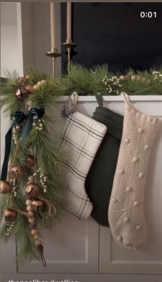 christmas stockings hanging on the mantle in front of a window with candles and garlands