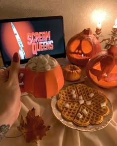 a table topped with pumpkins and waffles next to a computer screen that reads scream queens