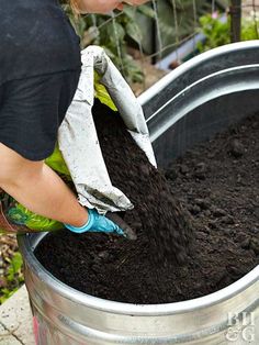 a woman is shoveling dirt into a large metal container with gardening gloves on it