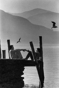 black and white photograph of two people sitting on a dock with seagulls in the background