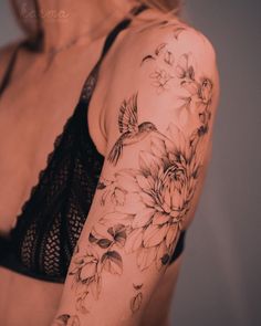 a woman's arm with flowers and a bird tattoo on her left arm, behind her is a bra