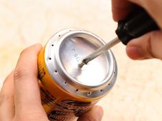 a person holding a can with a screwdriver in it